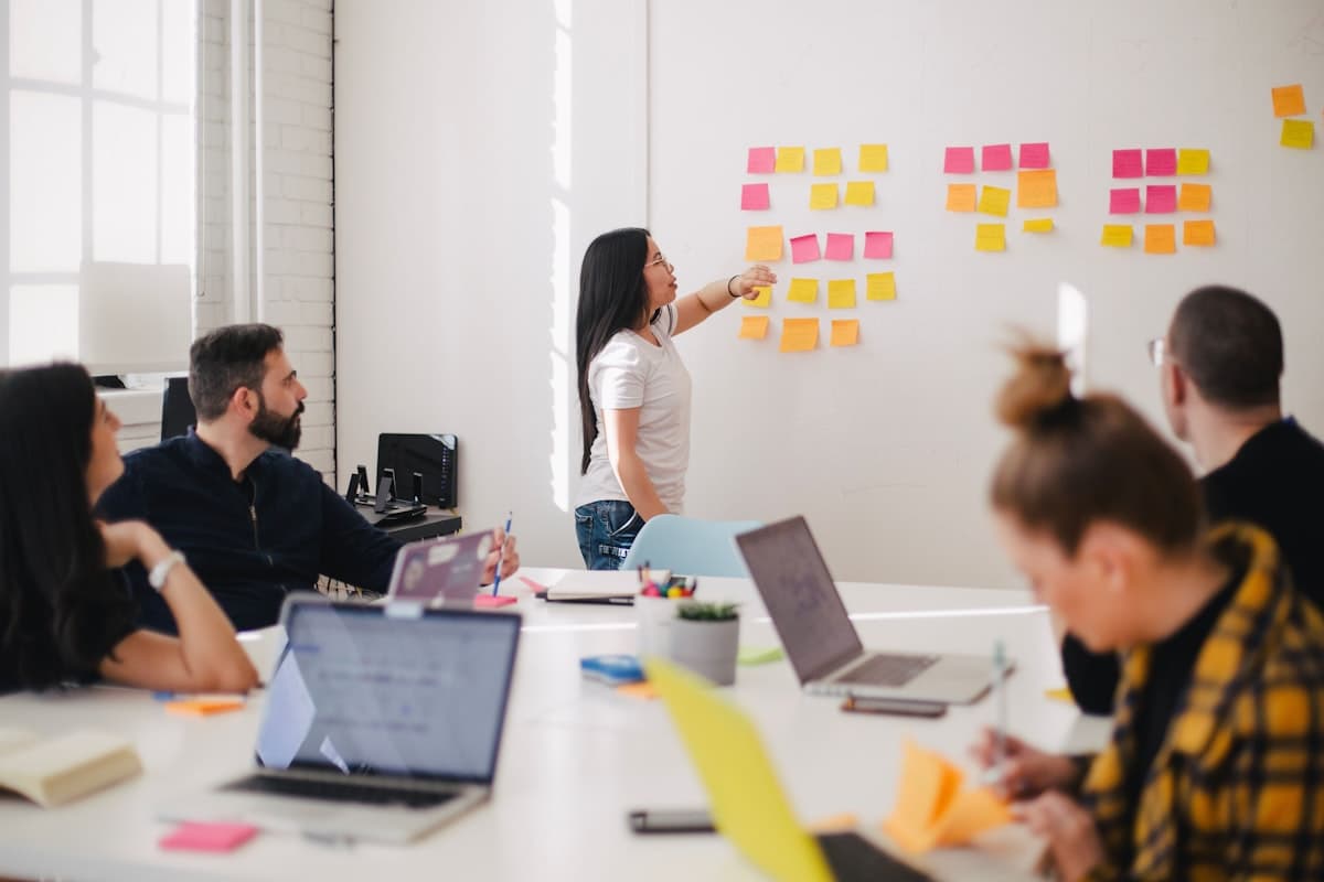 A trainer leading a team workshop at a whiteboard while the team follows on laptops